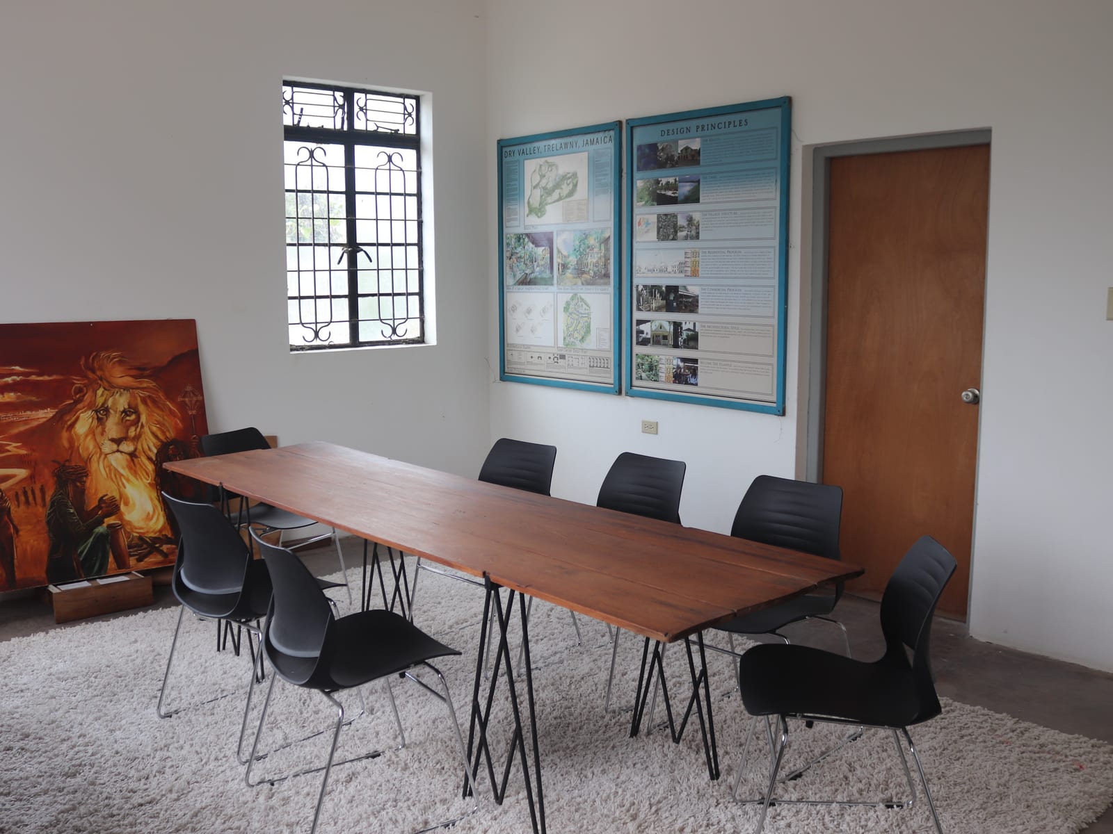 meeting room with long wood table, black chairs, shag rug and wall boards displaying project posters.