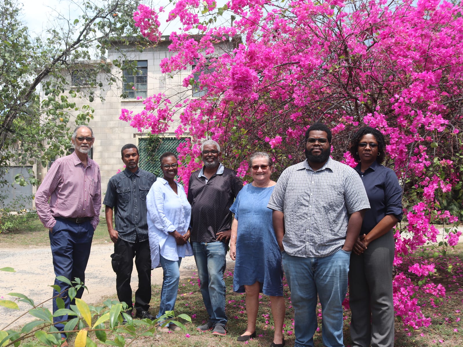 group portrait of seven people standing by bright pink bougainvillea in the office garden.