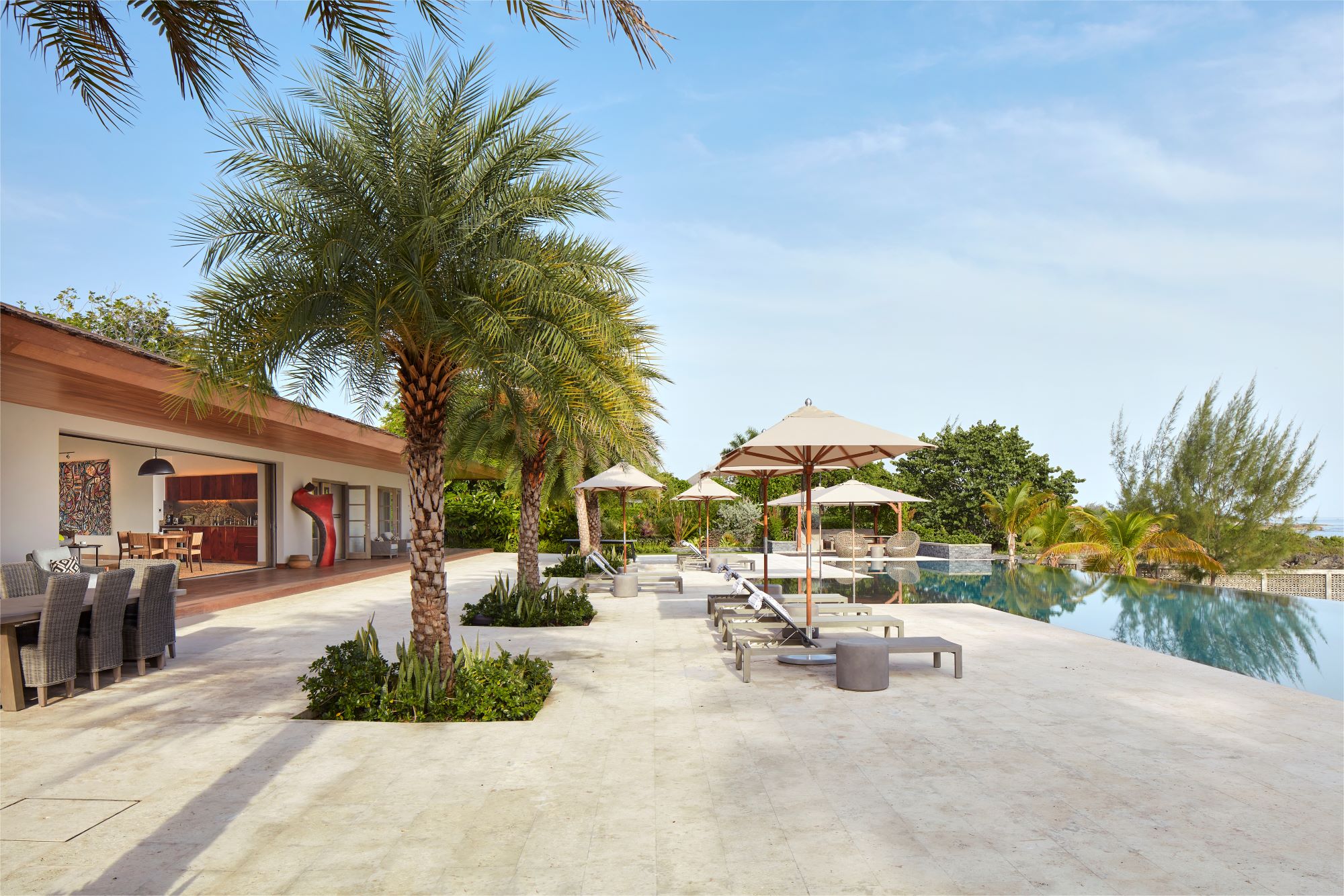 poolhouse, pool deck, large pool deck, pool, infinity pool, palm tree, dining, outdoor dining, open living, landscape, landscape chairs, lounge, entertainment, umbrella, blue sky