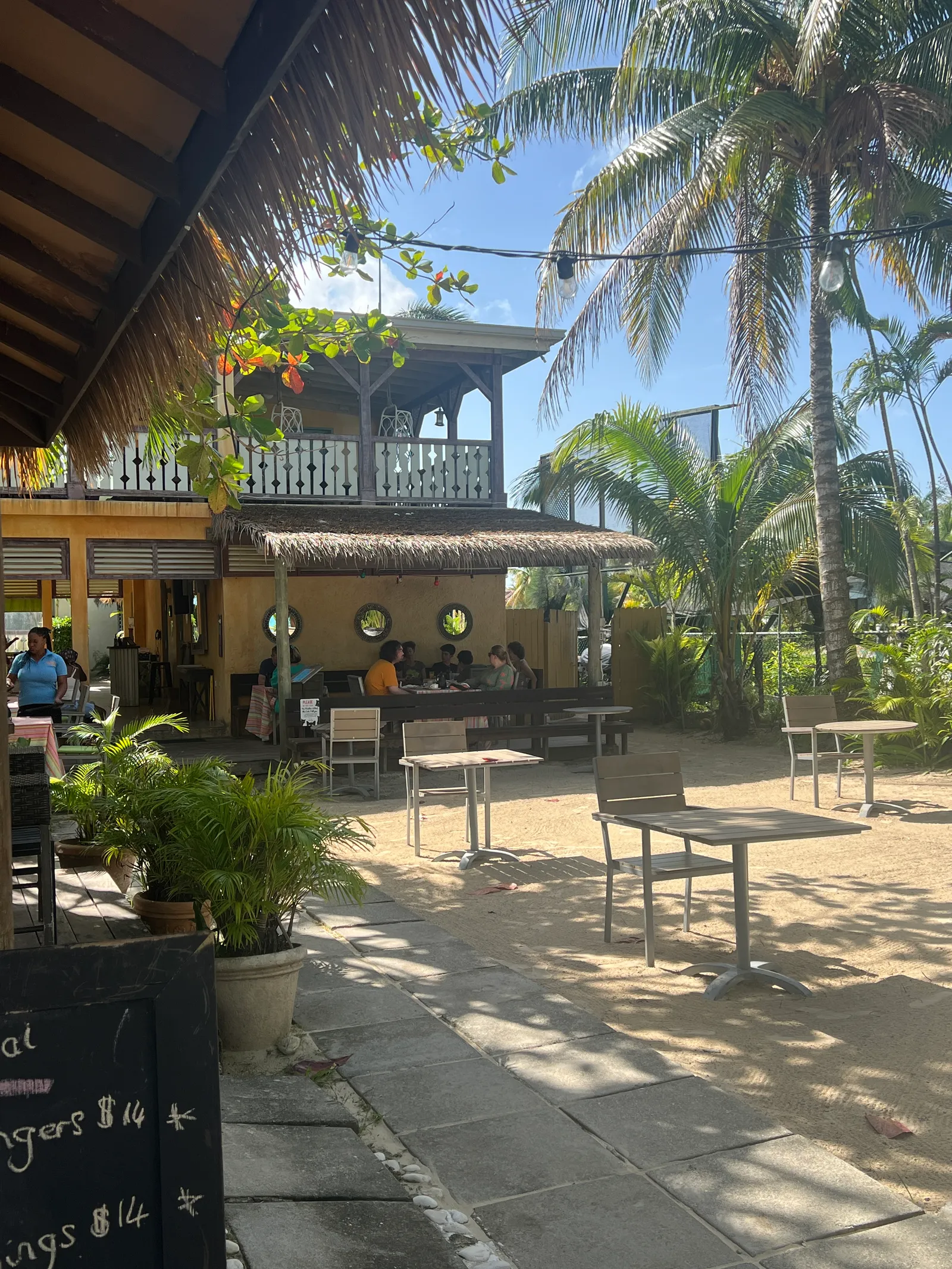 courtyard dining area by thatch eaves, porthole windows and guests seated under palms.