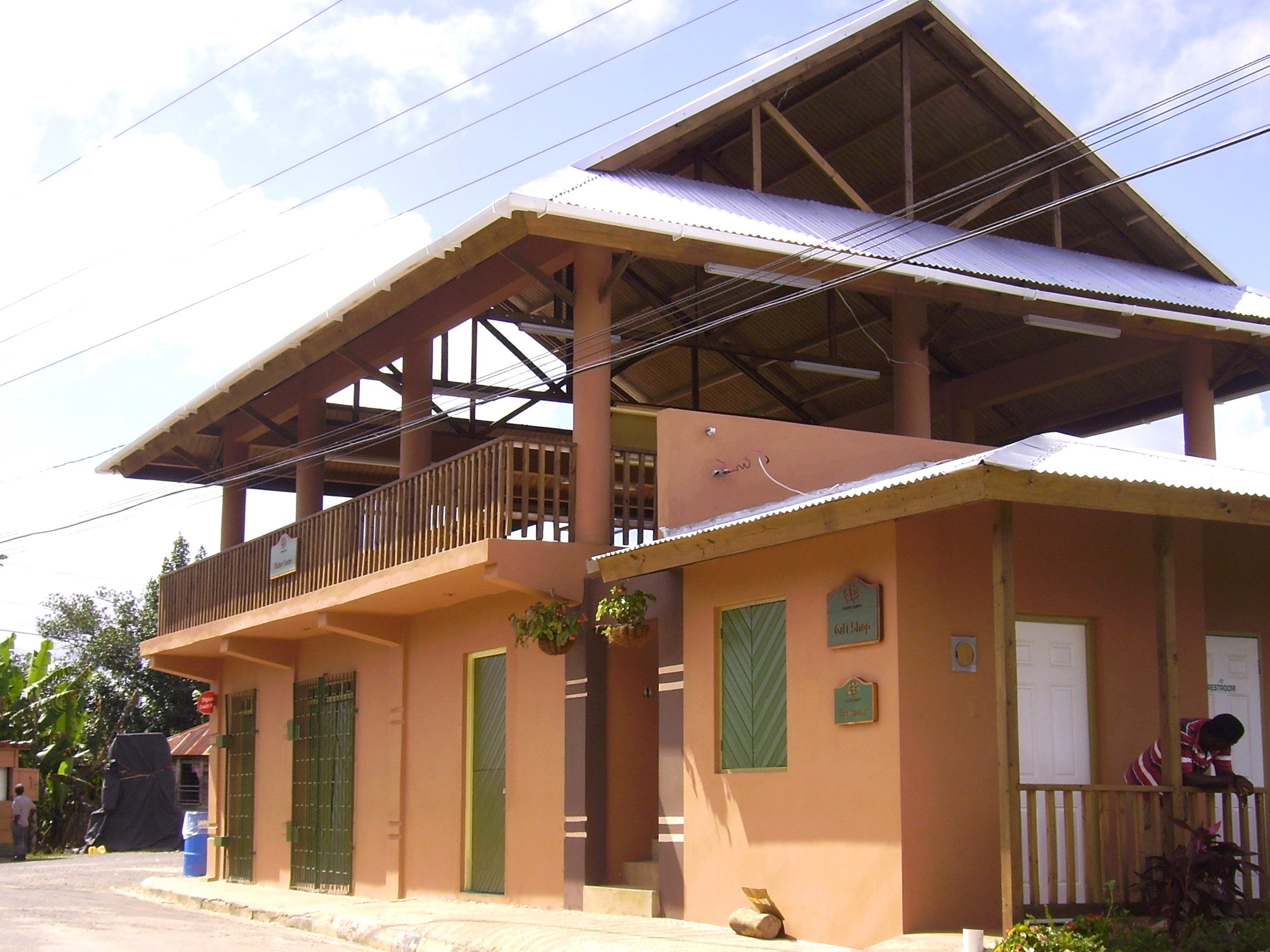 community building with open-air upper hall under twin metal roofs, timber railings and coral-tone stucco at street level.