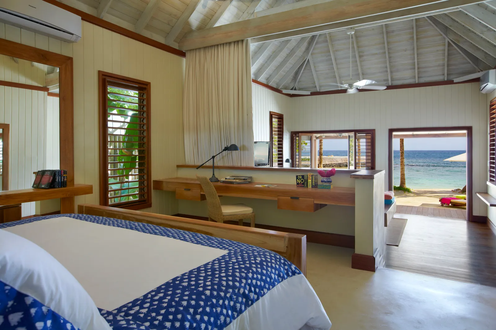 beachfront cottage interior with pitched timber ceiling, long desk and louvered windows, open doorway framing the Caribbean.
