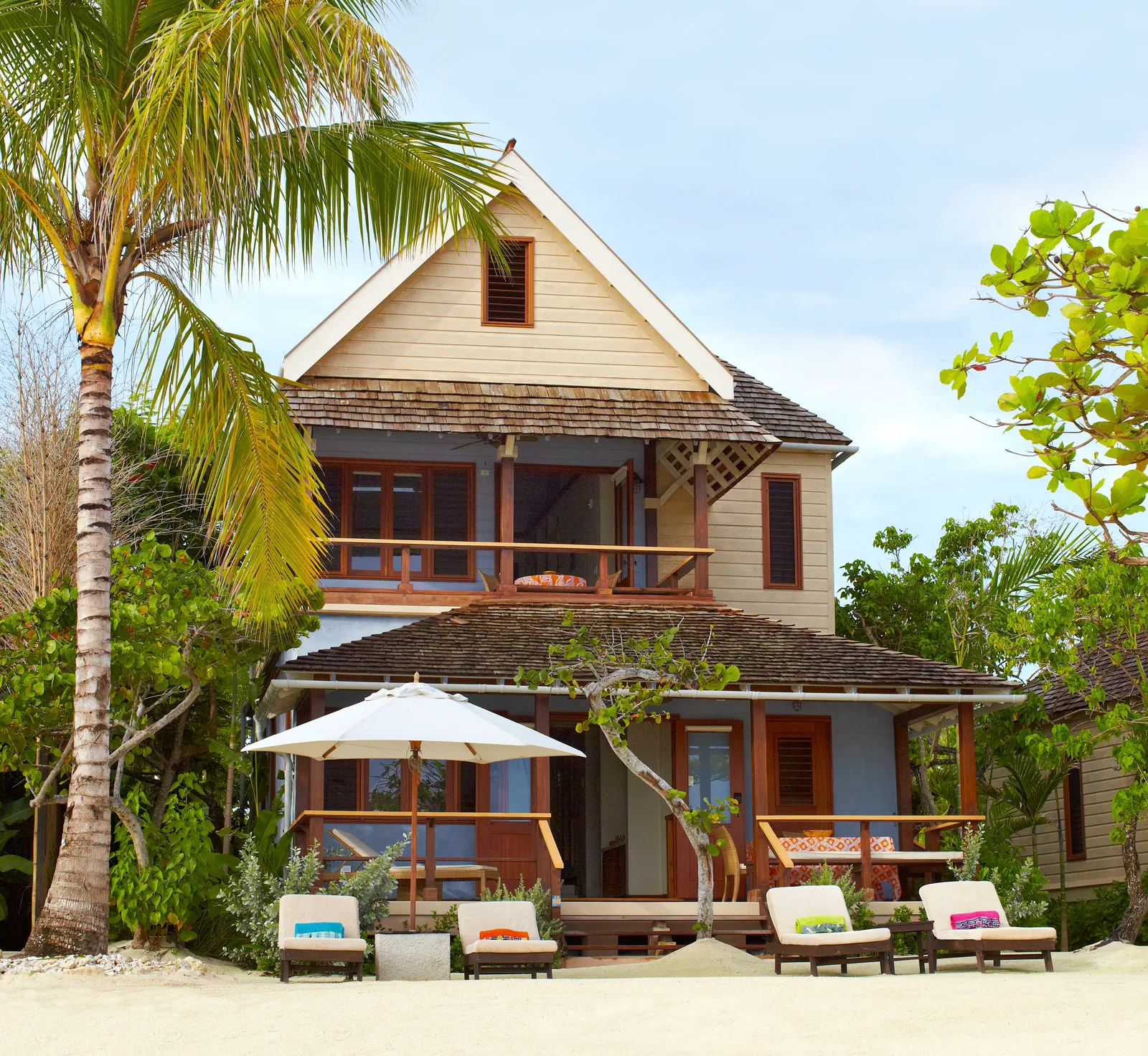 two-storey beachfront villa with shingled roof and deep verandahs, sun loungers and umbrella on the sand.