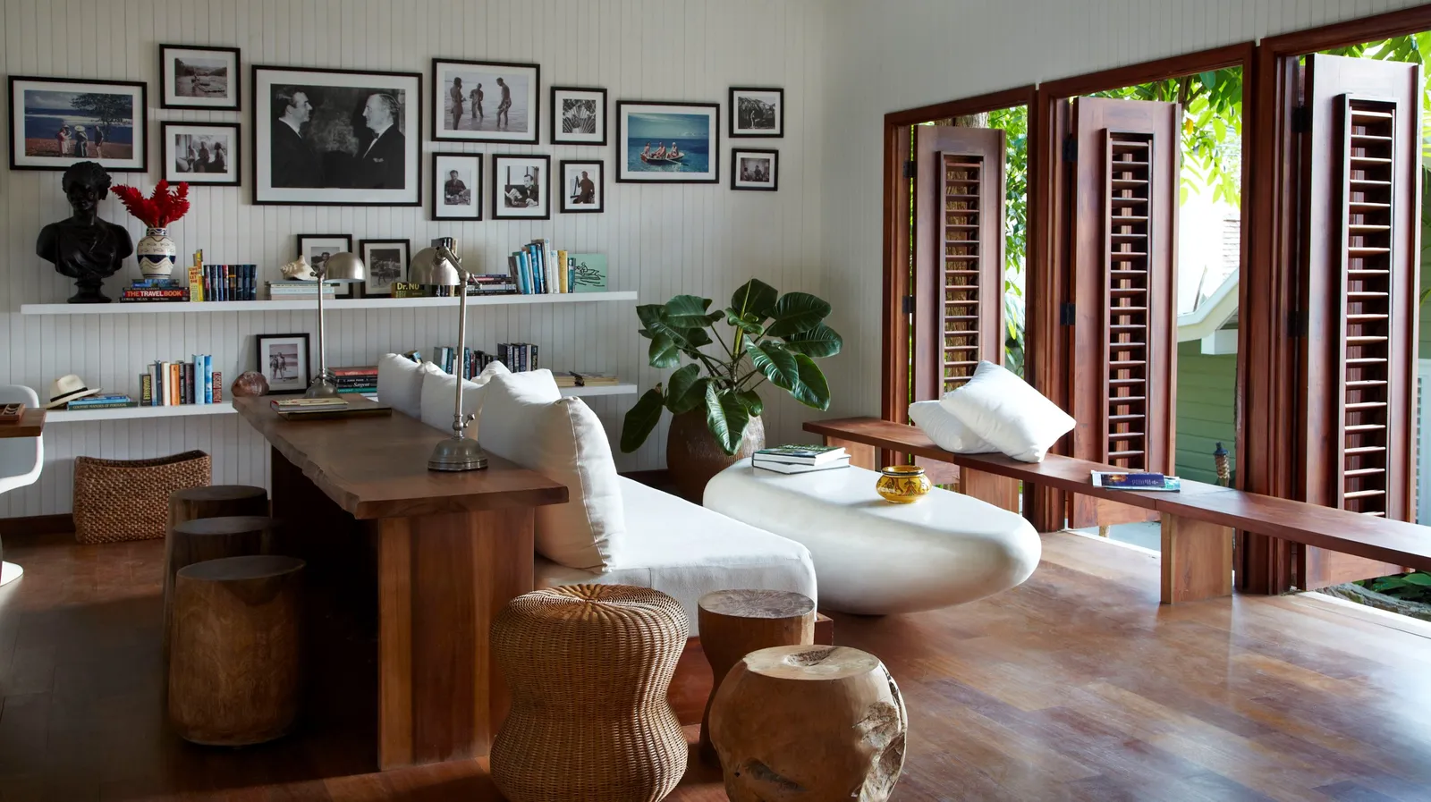 lounge and library with long timber desk, white sofas and gallery wall, louvered doors folded open to the garden.