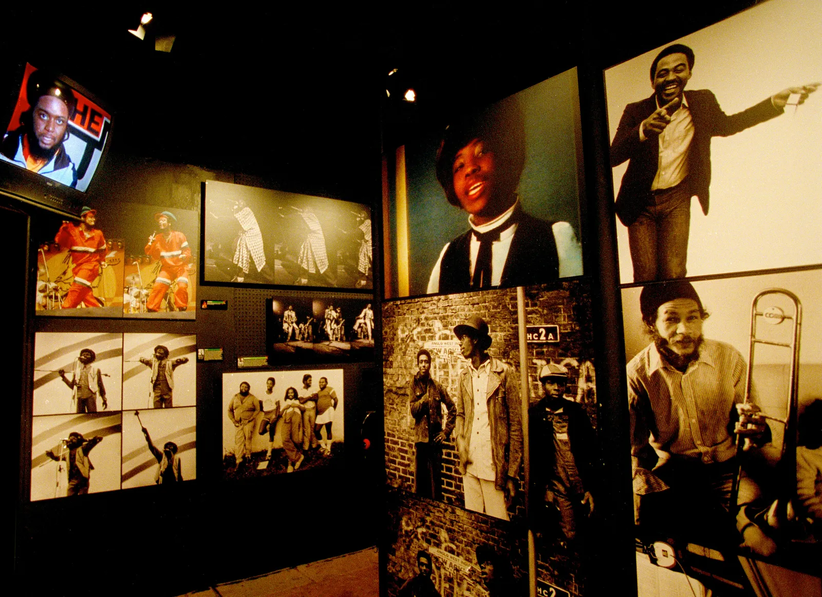 museum gallery wall of Jamaican music portraits and performance photos under low theatrical lighting.