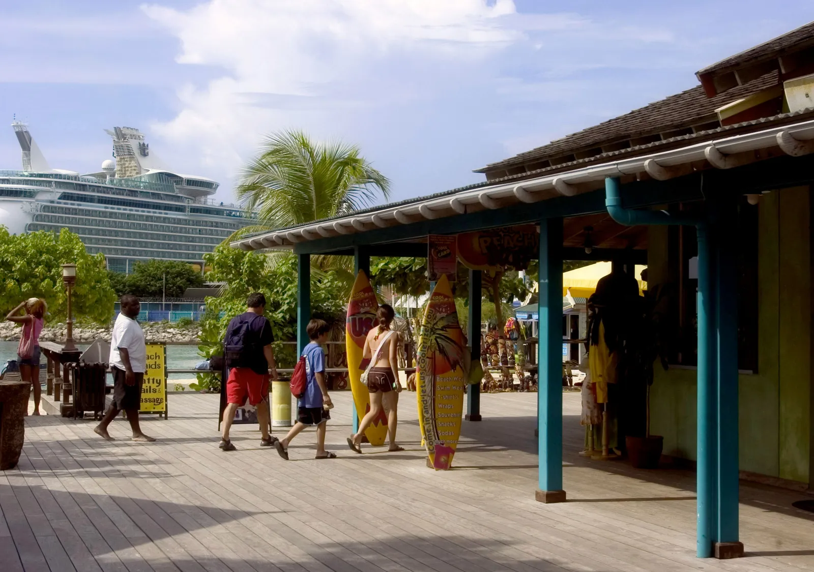 boardwalk of colorful shops with surfboard signs, cruise ship docked beyond the palms.