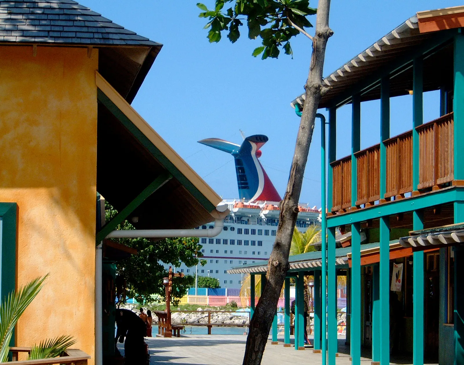 village lane between timber balconies and stucco walls, Carnival cruise funnel rising beyond the waterfront.