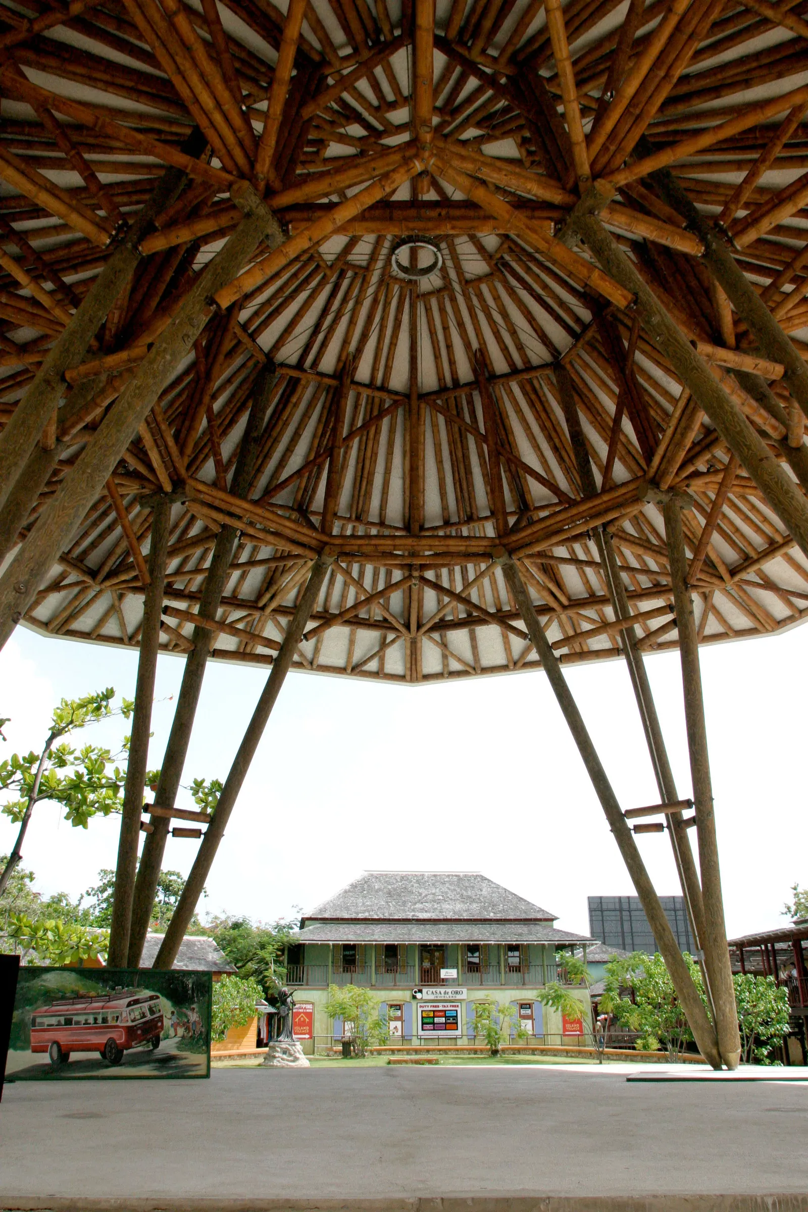 underside of the bamboo pavilion roof, radiating structure framing a historic timber house across the plaza.