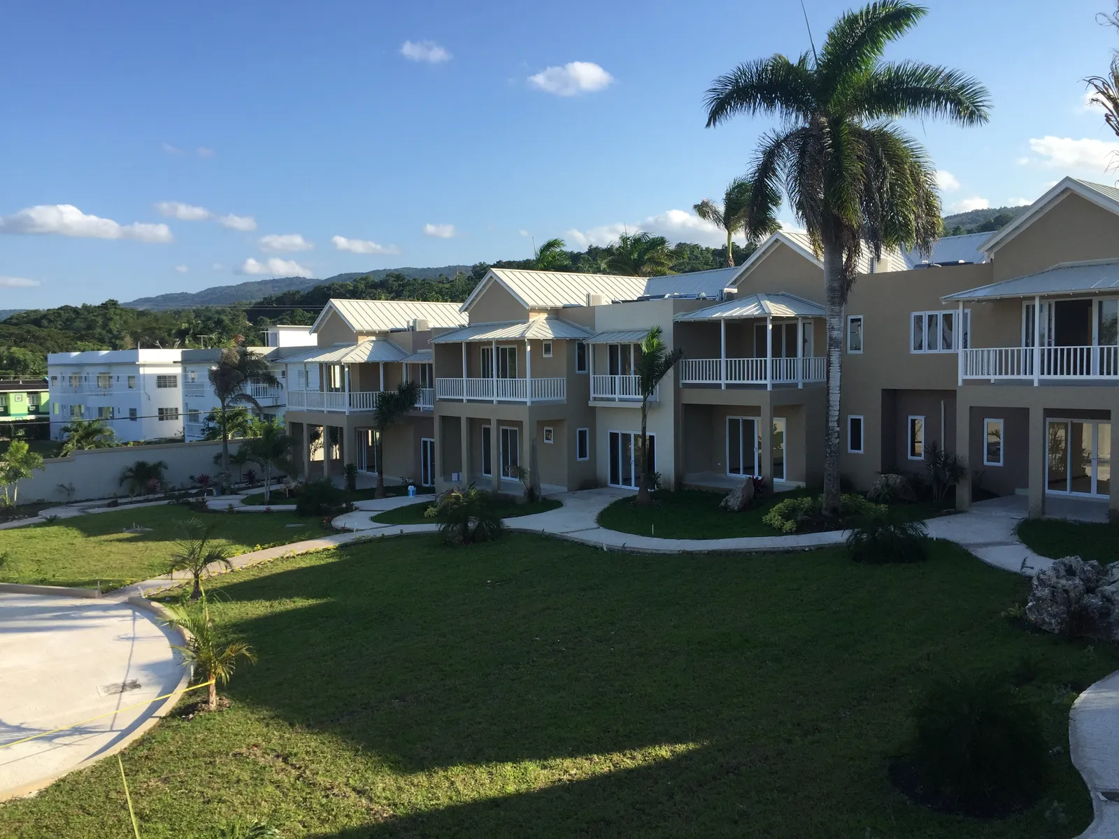 curving courtyard path past townhouses with balconies, boulders and red ti plants in fresh landscape.