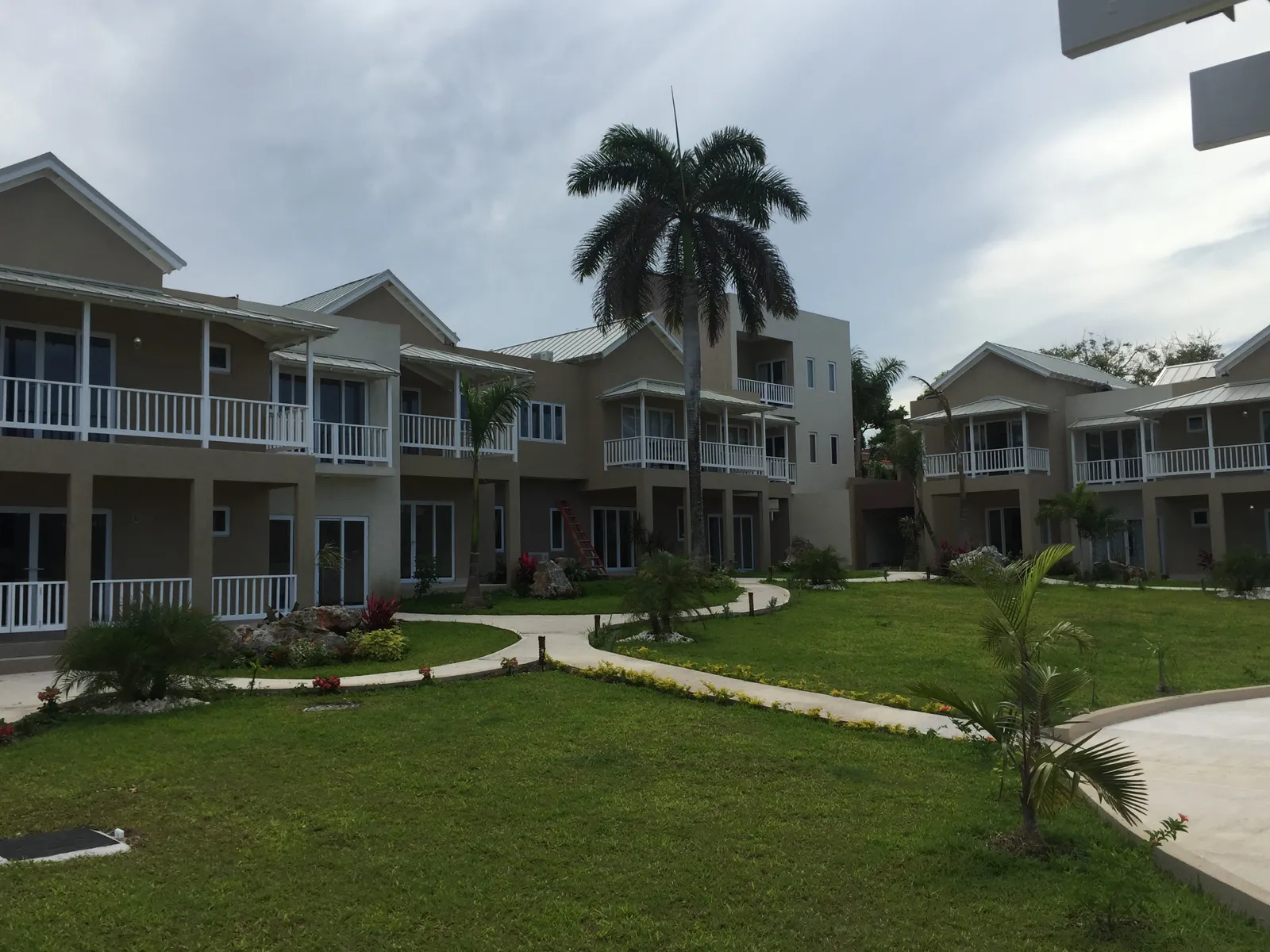 entry drive with paver roadway, covered parking to the right, gated entrance ahead, palms and gardens along the walk.