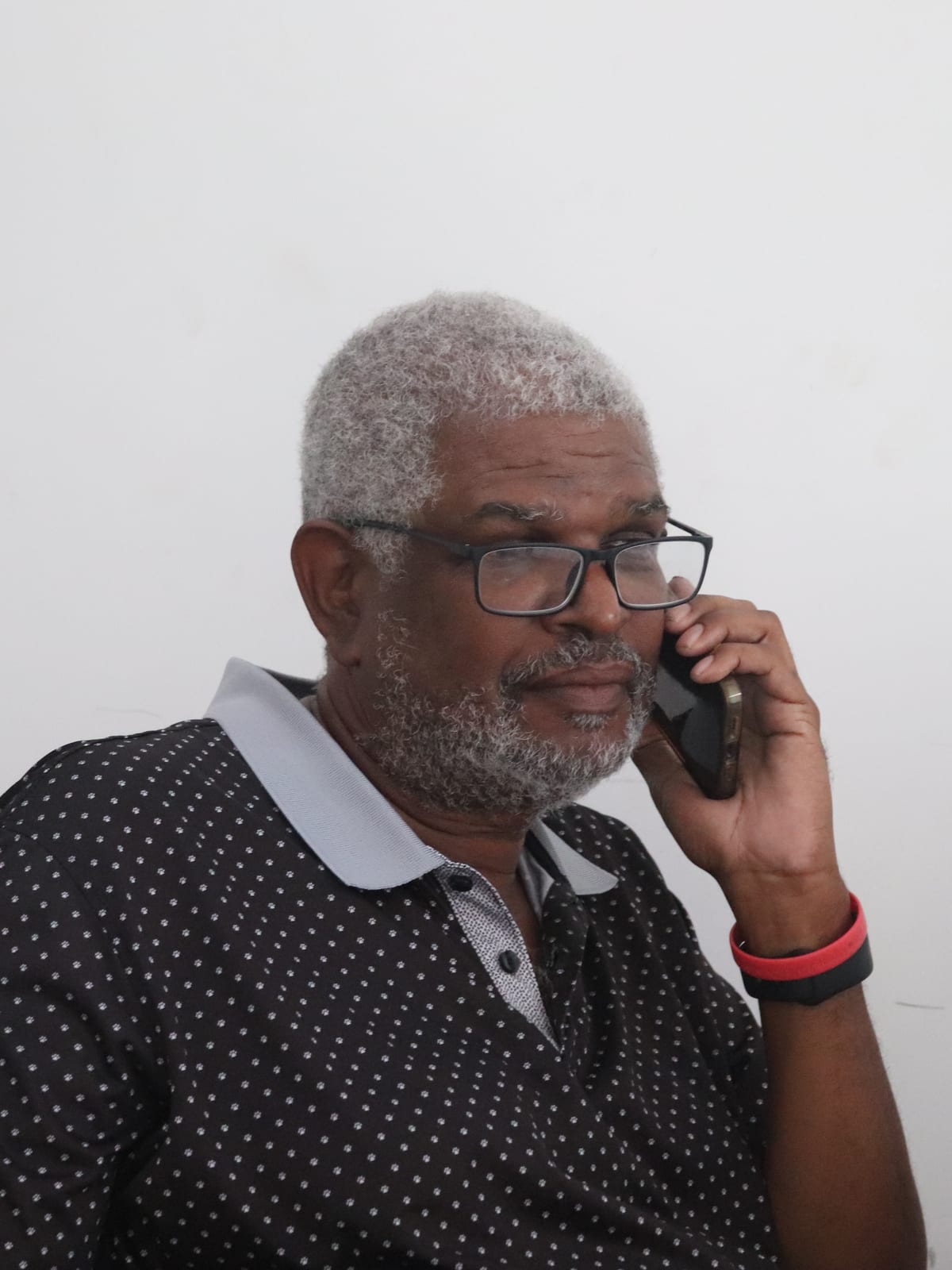 three-quarter portrait with salt-and-pepper hair and beard, speaking on phone, dark dotted polo.