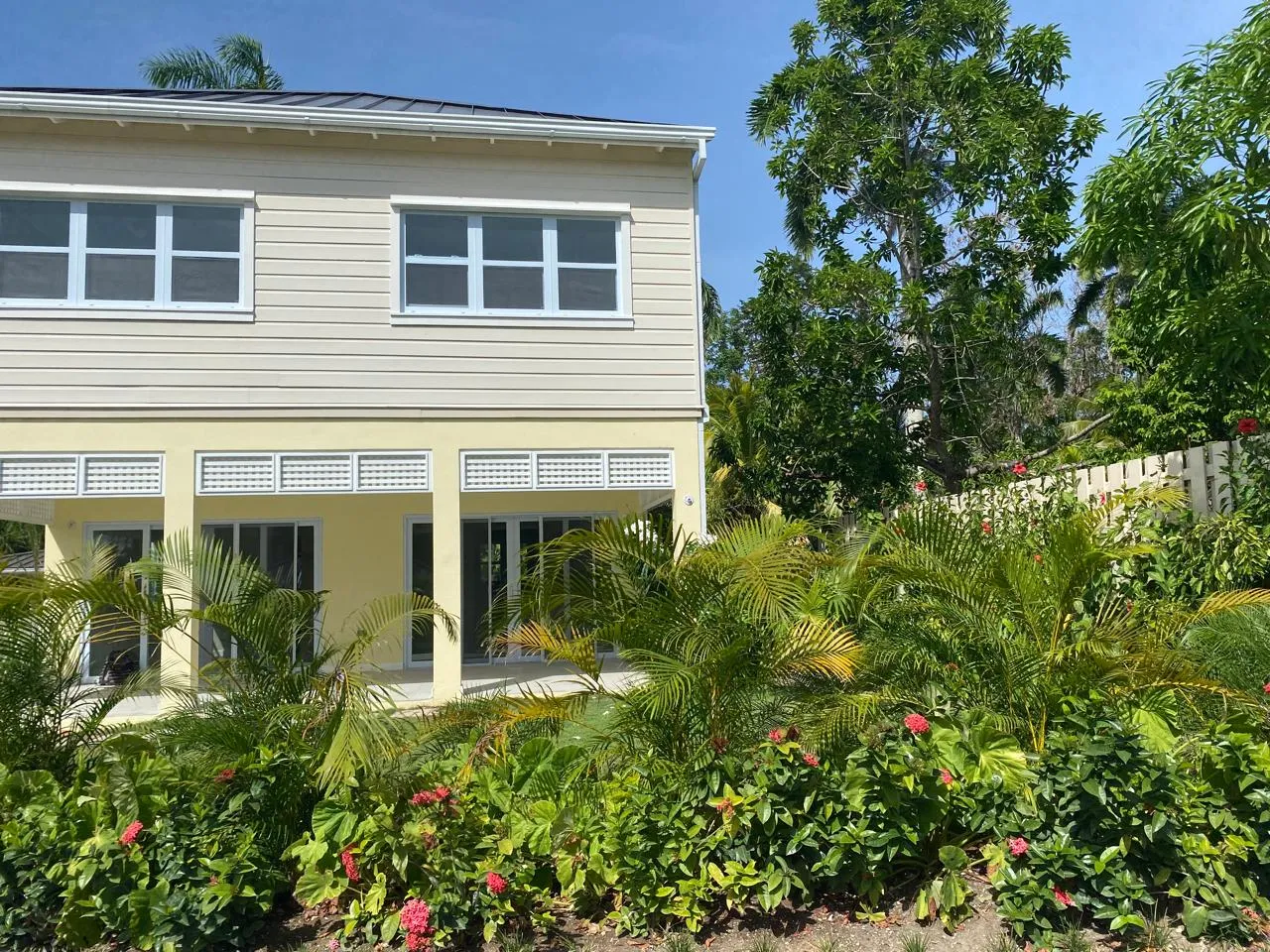rear elevation of a yellow two-storey block with shaded ground-floor terrace and louver panels, garden planting in front.