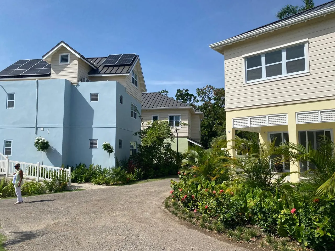 courtyard view with a building carrying roof-mounted solar panels beside a yellow block, landscaped drive and gardens.