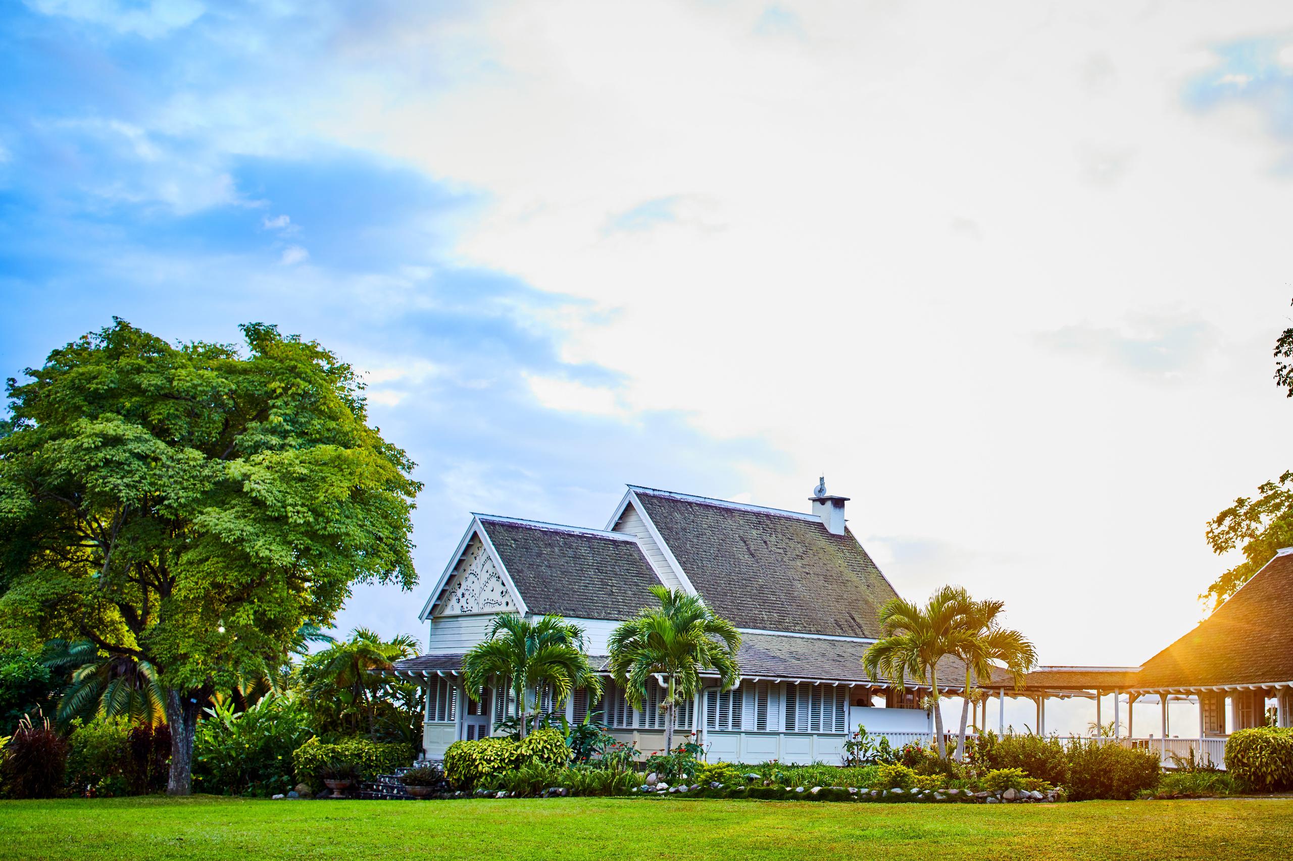 great house with fretwork gables and wraparound verandah set on a wide green lawn at golden hour.
