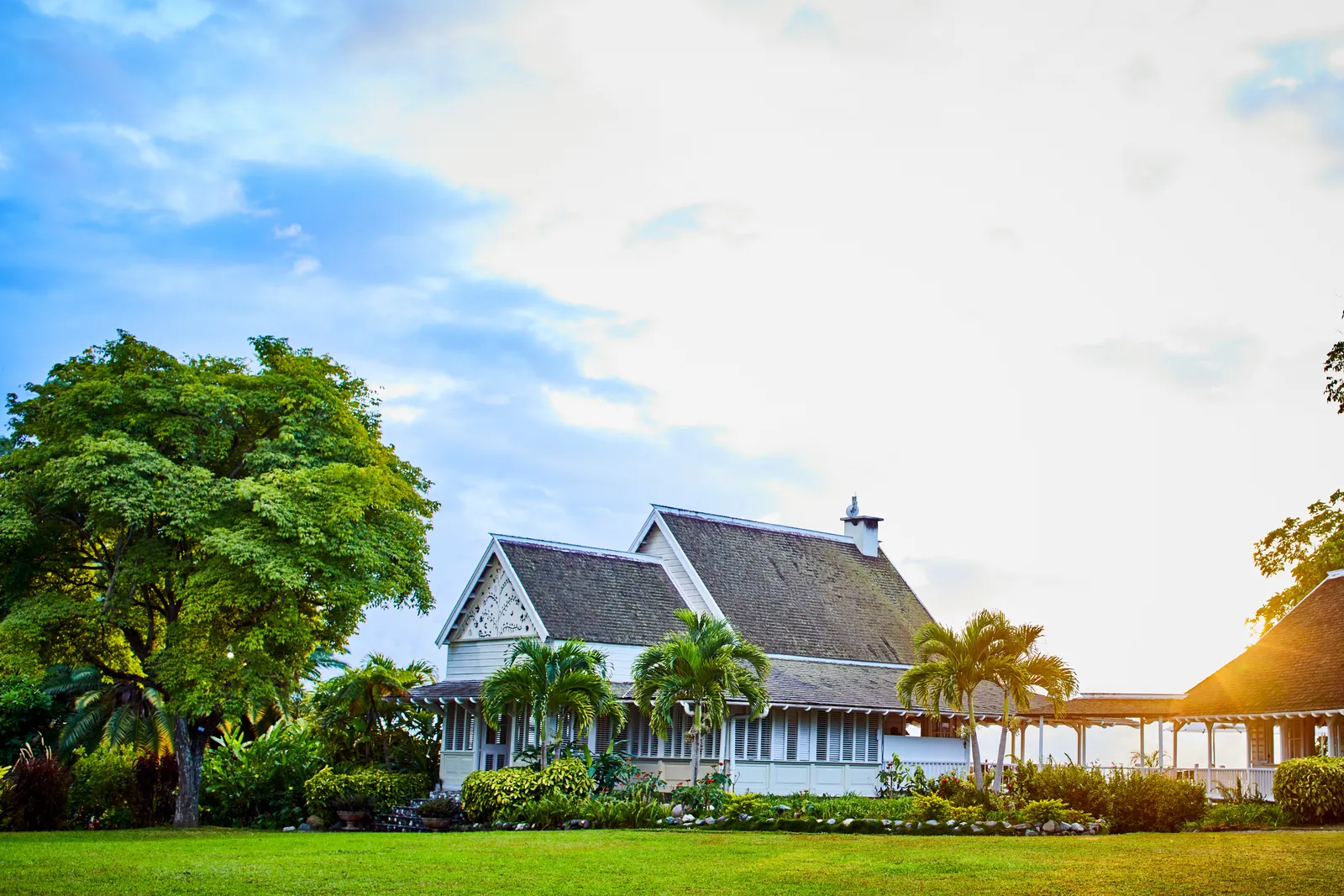 great house with fretwork gables and wraparound verandah set on a wide green lawn at golden hour.