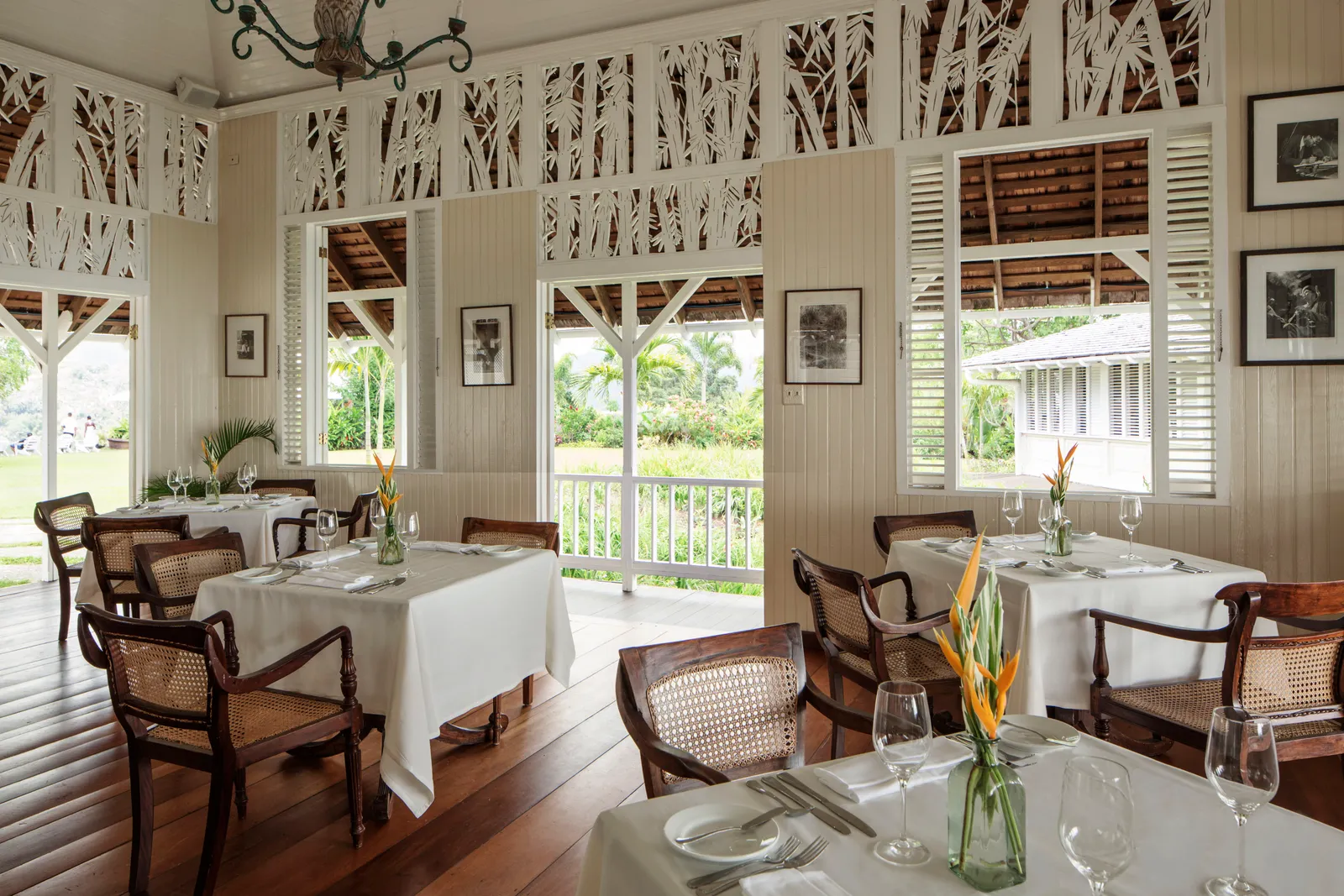 dining room with cane chairs and white tablecloths, carved fretwork screens and open doors to verandah and gardens.